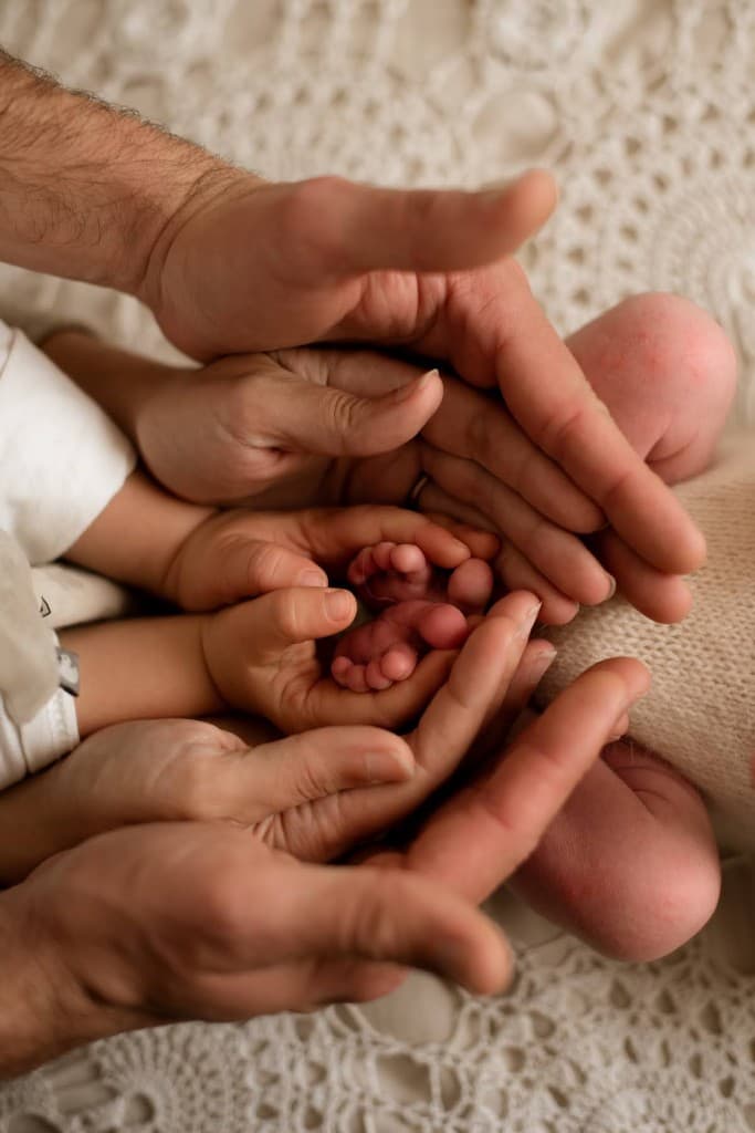 Mains de parents et fratrie autour des pieds d’un bébé